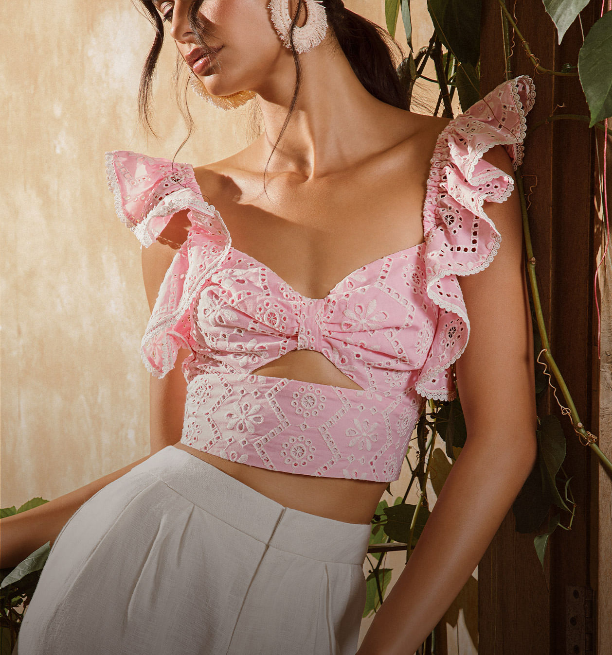 Foto en detalle de modelo usando blusa corta en hoja rota rosa y pantalón blanco de la marca Studio F